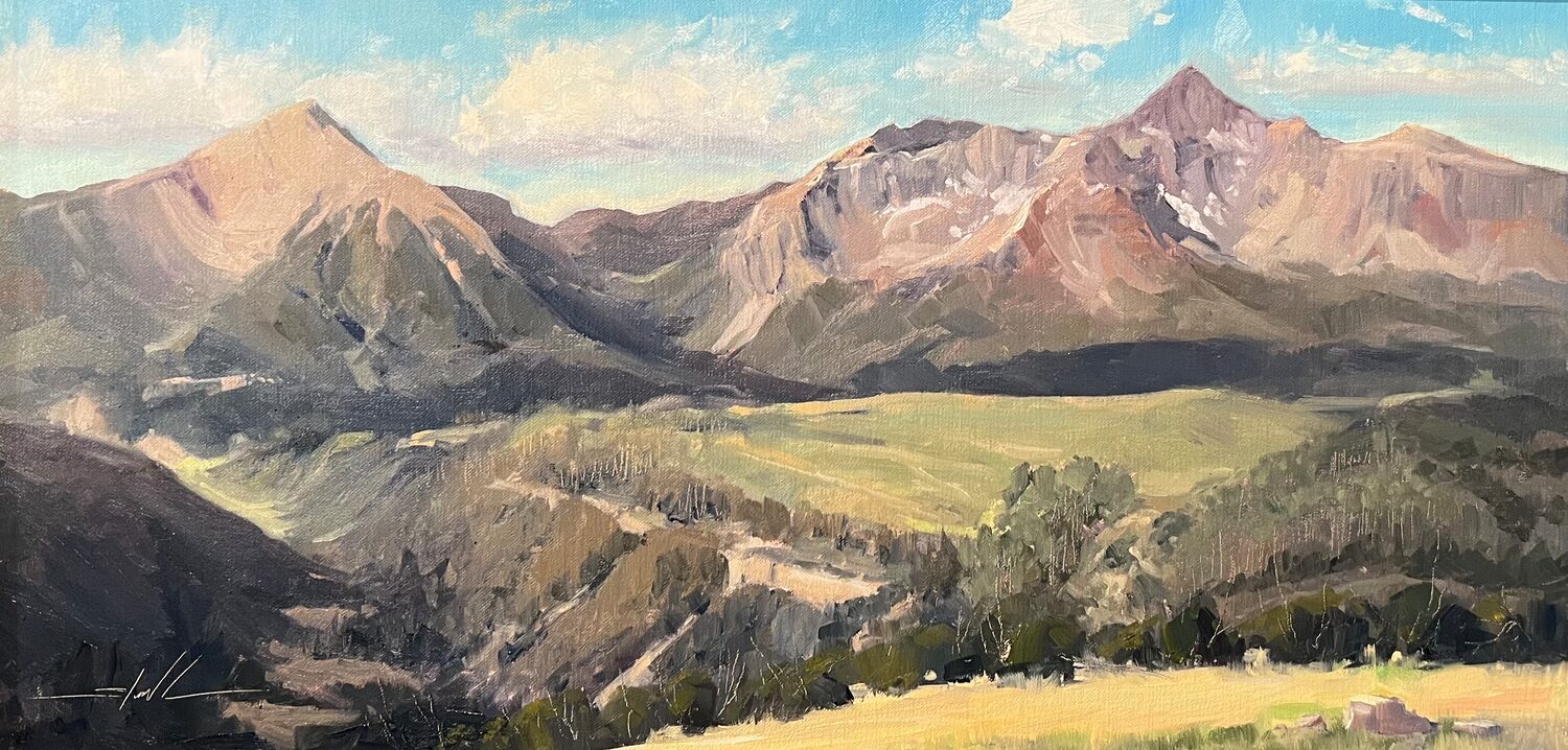 A painted landscape of distant mountains under a blue sky with clouds, sunlit grassy fields, and a valley with shadows in the foreground. 15th Annual PleinAir Salon Art Competition