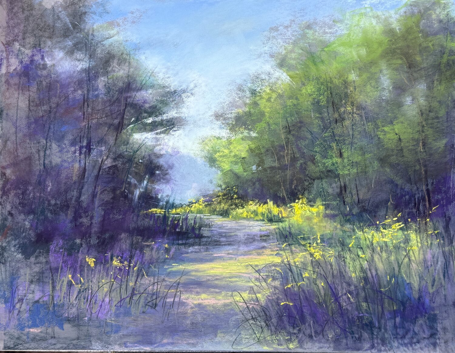 A sunlit forest path winds through green trees and tall grasses with yellow wildflowers, under a bright blue sky with soft, wispy clouds. 15th Annual PleinAir Salon Art Competition